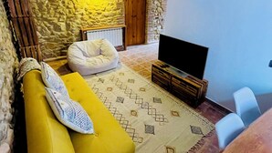 A cozy living room with a stone wall, a yellow sofa, a patterned rug, and a television. - Village house in Palamós (Palamós)