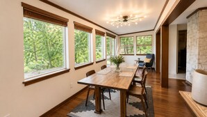 Un coin repas avec une table en bois, des chaises, un vase agrémenté de plantes et de grandes fenêtres donnant sur la forêt.