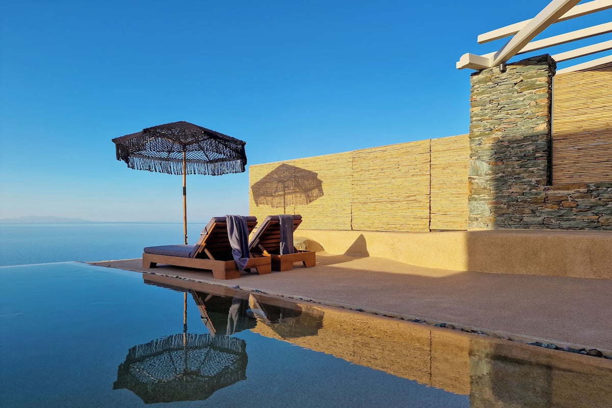 En infinitypool med solstolar och ett parasoll, en stenmur och en fri utsikt över horisonten.