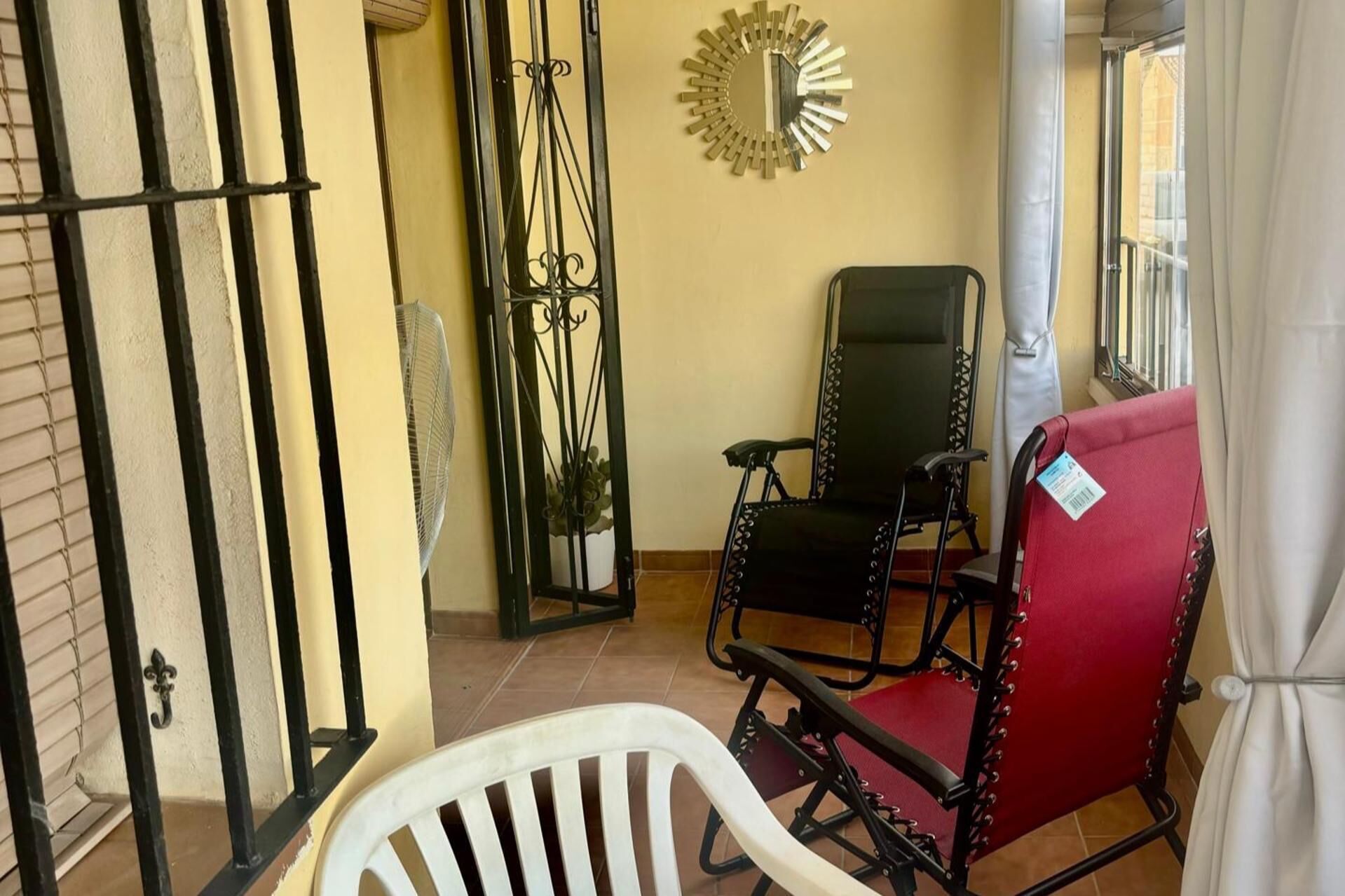 Een kamer met een witte plastic stoel, een rode fauteuil en een zwarte stoel met metalen poten.