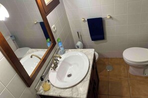 Um banheiro com pia branca, espelho, vaso sanitário e porta-toalhas.