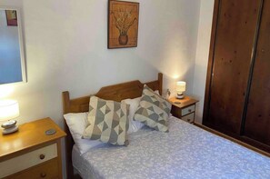 Cama bem arrumada com almofadas estampadas, luminária de cabeceira e cabeceira de madeira.