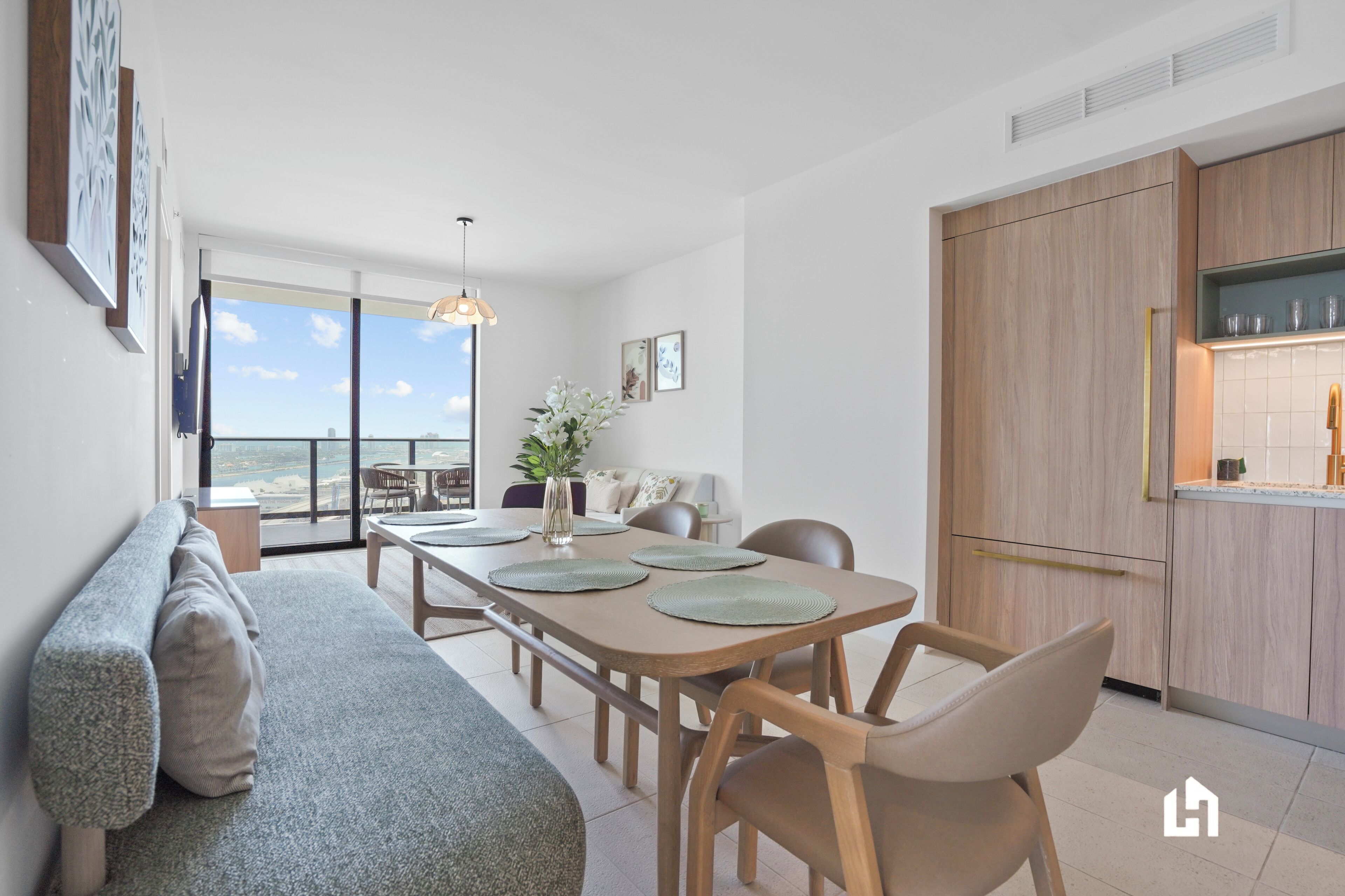 A modern dining area with a wooden table, chairs, and a bench. There is a view of the outdoors through large windows.