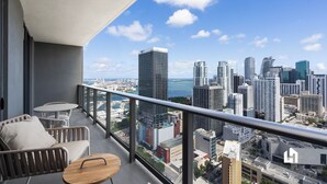 A balcony with a city view, furnished with a sofa and a table, overlooking a skyline with high-rise buildings. - Stylish Apartments with Partial Ocean Views in Downtown (Miami)