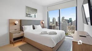 A modern hotel room with a large bed, bedside tables, a mounted TV, and a city view. - Stylish Apartments with Partial Ocean Views in Downtown (Miami)