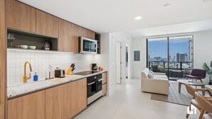 A modern kitchen with wooden cabinets, a built-in microwave, and a large window overlooking a cityscape. - Stylish Apartments with Partial Ocean Views in Downtown (Miami)