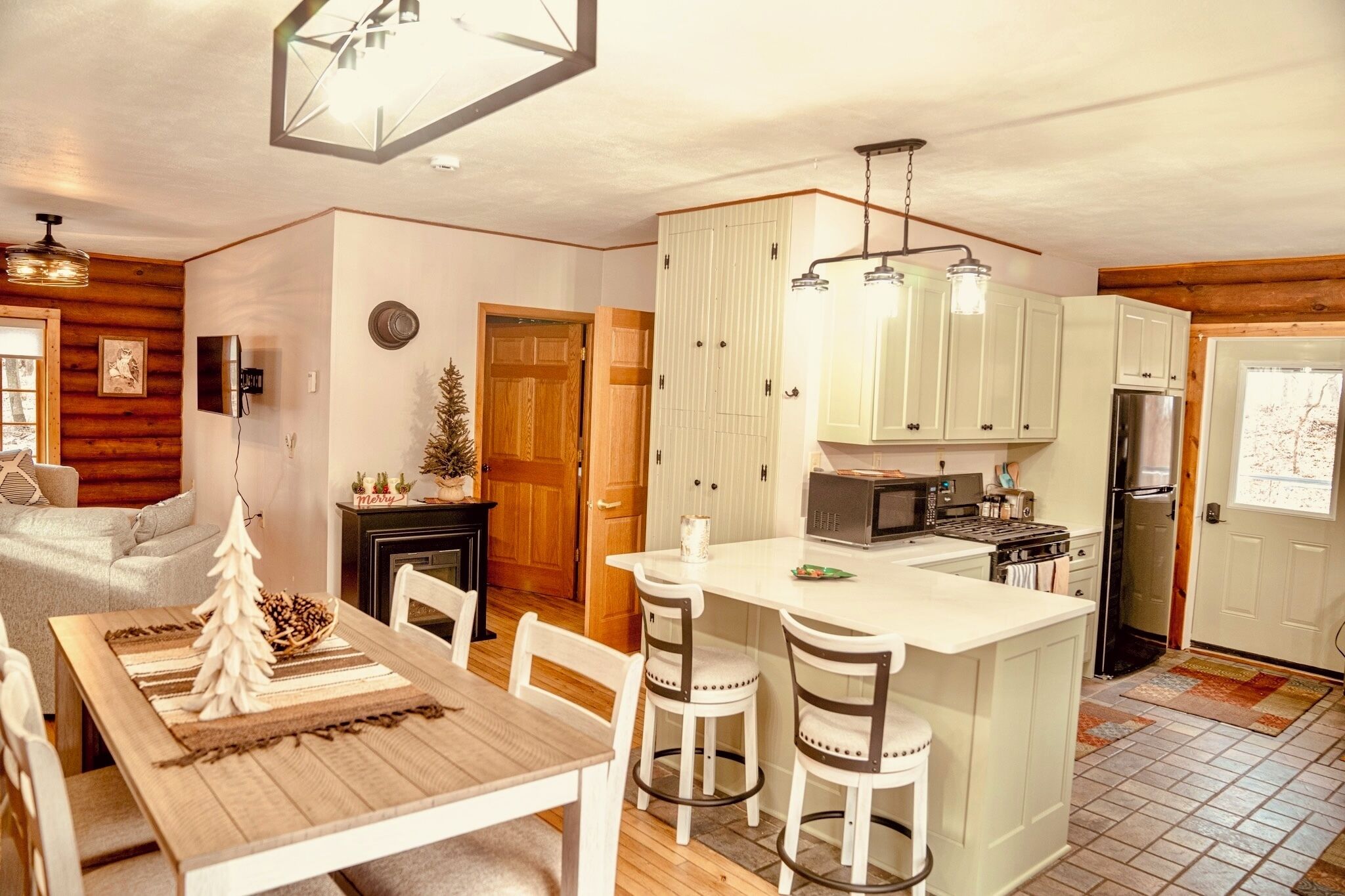 A cozy kitchen with wooden cabinets, a central island, and a dining area with a Christmas tree decoration.