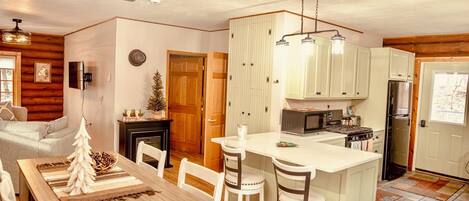 A cozy kitchen with wooden cabinets, a central island, and a dining area with a Christmas tree decoration.