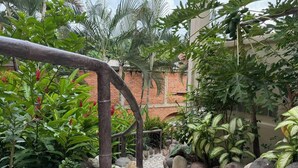 A garden pathway with a rustic wooden archway, surrounded by lush tropical plants and a stone-tiled floor.