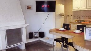 Un espace de vie compact comprenant une cheminée, un coin repas, une cuisine et un téléviseur à écran plat fixé au mur.
