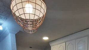 Un coin repas avec une table dressée pour quatre personnes, une cuisine en arrière-plan et un luminaire suspendu.