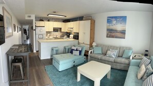 A compact living space with a kitchenette, a sofa, a coffee table, and a painting of a beach scene. - Relisted!Ocean Blk, Bay&Ocean view, steps to beach best food & bars 2 Full Baths (Ocean City)