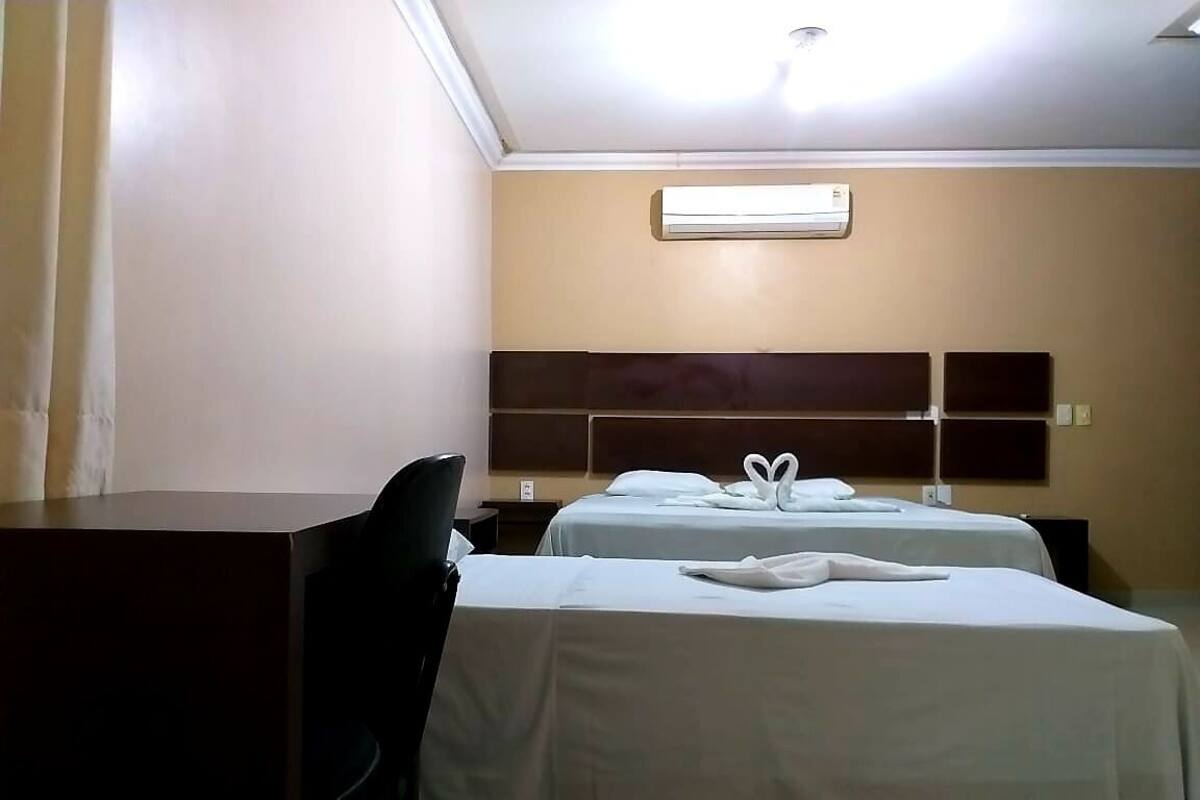 Quarto de hotel com duas camas, uma escrivaninha e um ar condicionado na parede.