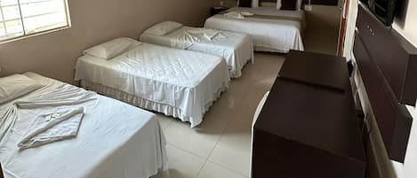 Een hotelkamer met drie eenpersoonsbedden, een bureau en een televisie.