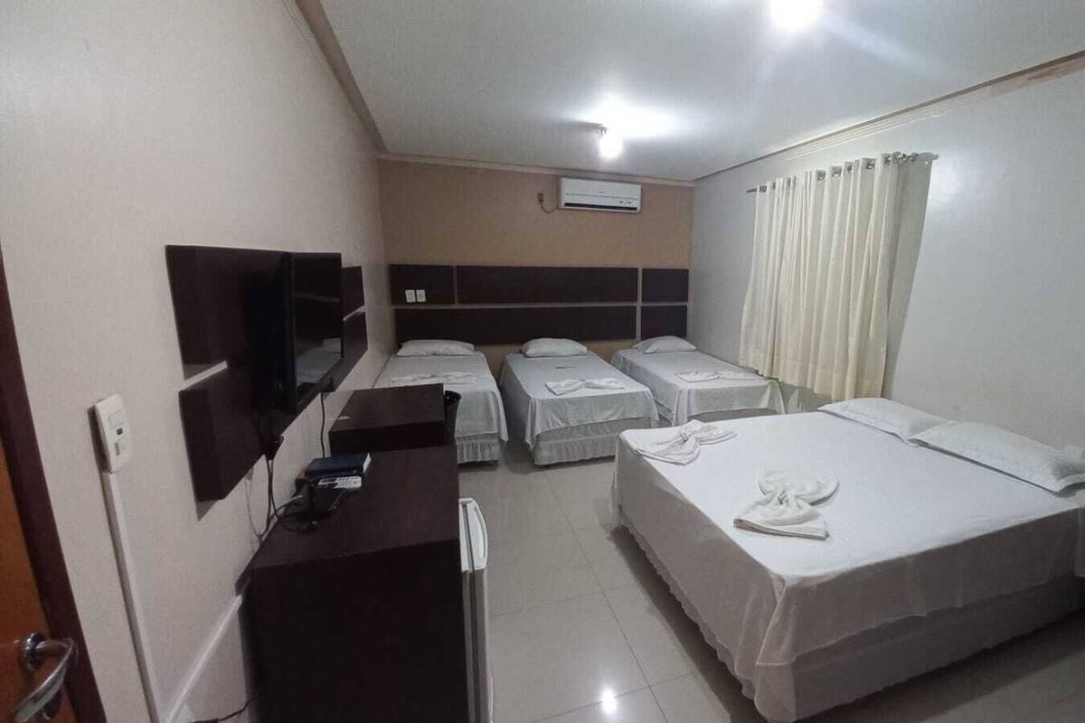 Quarto de hotel com duas camas de solteiro, uma secretária com cadeira, televisão de tela plana na parede e janela com cortinas.