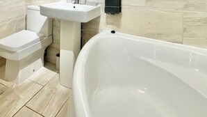 A bathroom with a bathtub, toilet, and sink. - Spacious 4-Bedroom Home | Driveway & Garden (Greater London)