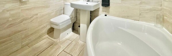 A bathroom with a bathtub, toilet, and sink. - Spacious 4-Bedroom Home | Driveway & Garden (Greater London)