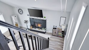 Una sala de estar moderna con chimenea, un televisor de pantalla plana y una escalera que sube a otro nivel.