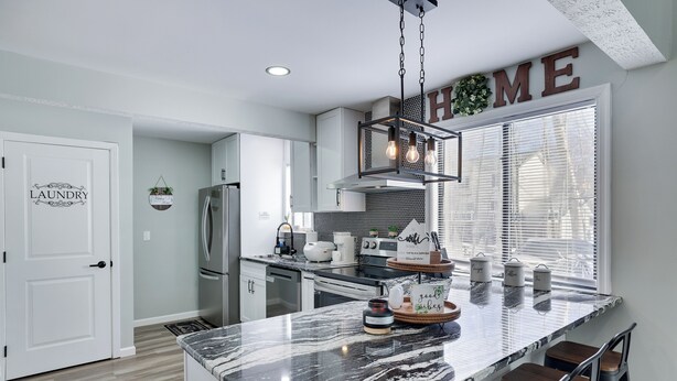 Una cocina moderna con una isla de mármol, taburetes de bar y un letrero que dice 'HOME' sobre la ventana.