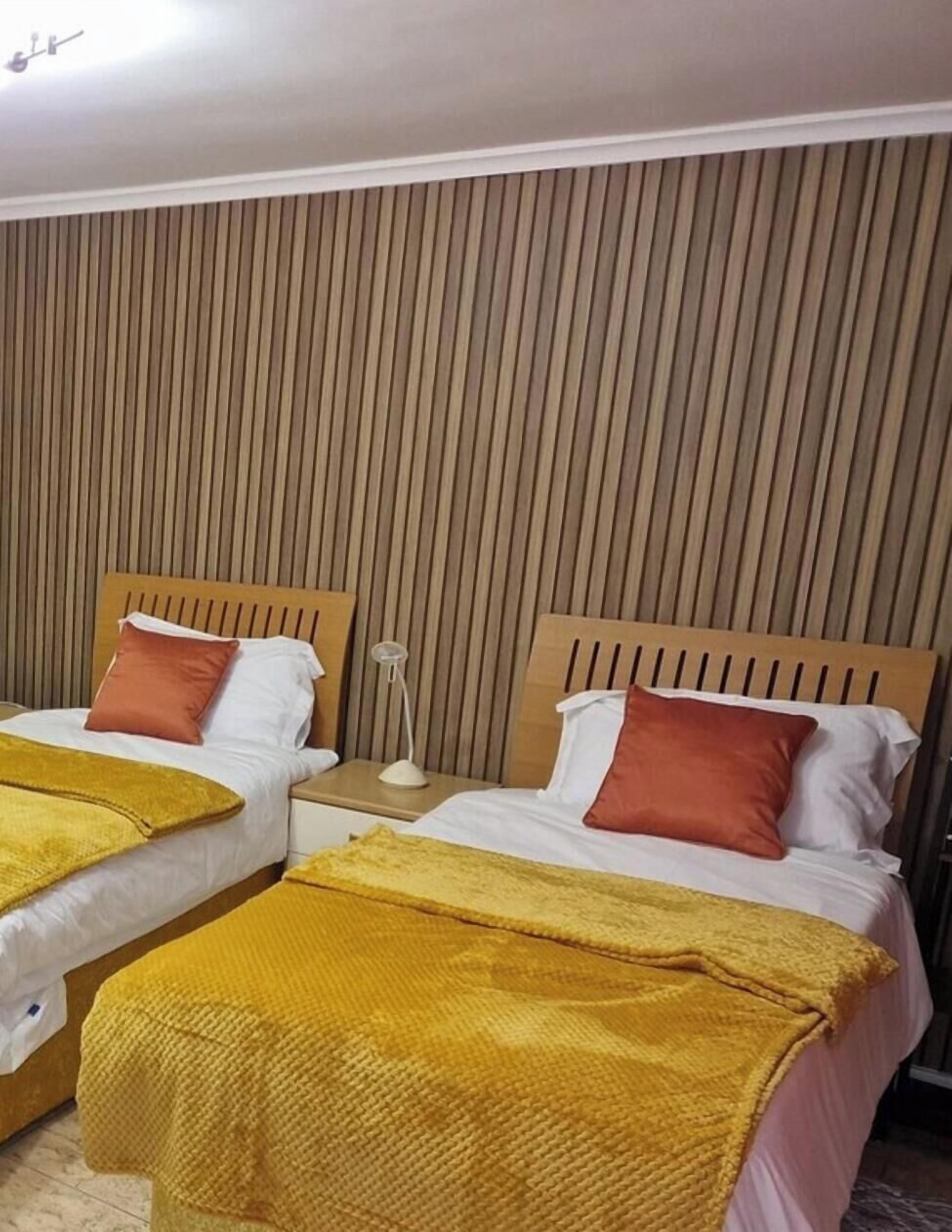 Habitación de hotel con dos camas, cabeceros de madera, una mesita de noche con lámpara y pared a rayas.