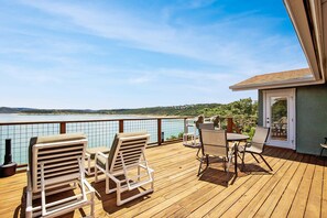 A wooden deck with lounge chairs and a table, overlooking a body of water and hills.