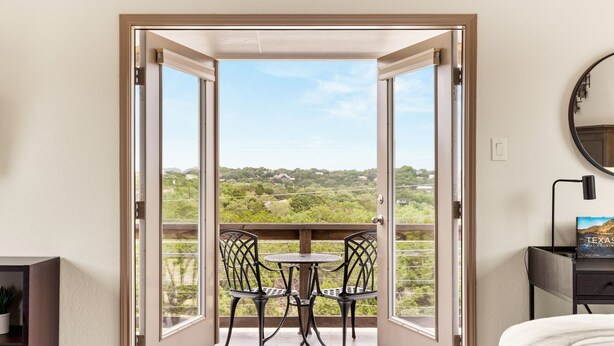 A room with a balcony, a bed, a table with chairs, and a view of greenery and buildings. - Book Labor Day | Hot Tub + Grill | Pet-Friendly! (Canyon Lake)
