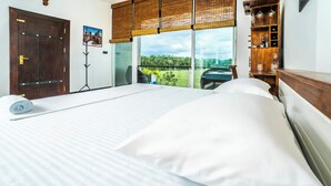 A bedroom with a large bed, a wooden wardrobe, a window with a view of greenery, and a door with a cityscape picture. - The Quale Villa (Galle)