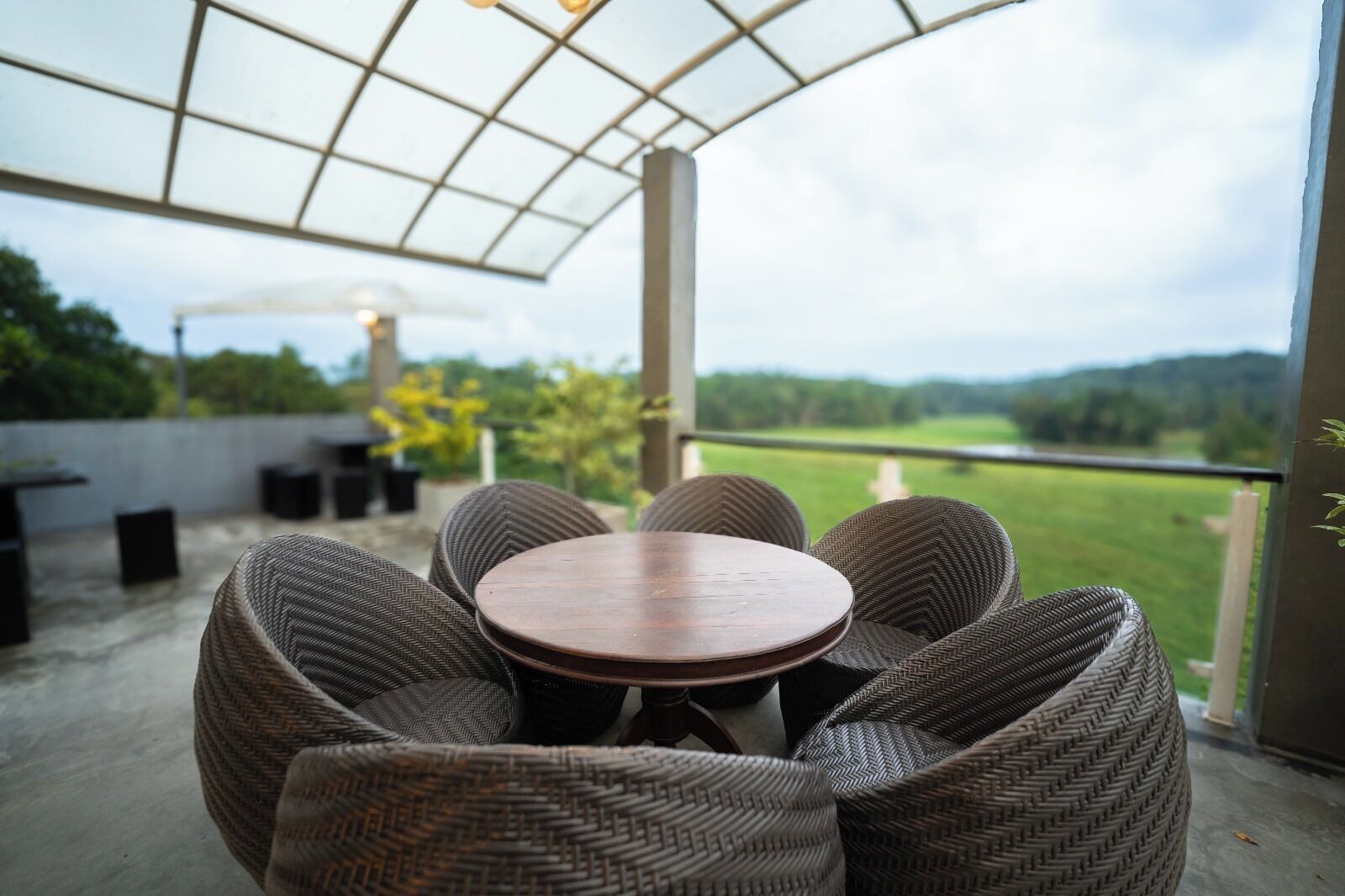 Un patio al aire libre con mobiliario de mimbre y una mesa, con vistas a un paisaje verde.