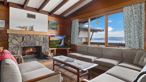 Een gezellige woonkamer met een stenen openhaard, een groot raam met uitzicht op het meer en een comfortabele zithoek.