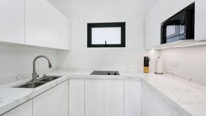 Una cocina moderna con armarios blancos, un lavamanos de acero inoxidable, una ventana con marco negro y un microondas sobre la encimera.