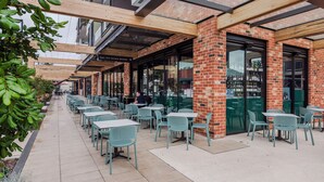 An outdoor café with tables and chairs, brick walls, and large windows.