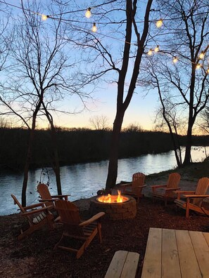 A lakeside seating area with wooden chairs and a fire pit. - The Floy at High Bank – Charming Elk Riverfront Tiny Cabin in Scenic Noel, MO (Noel)