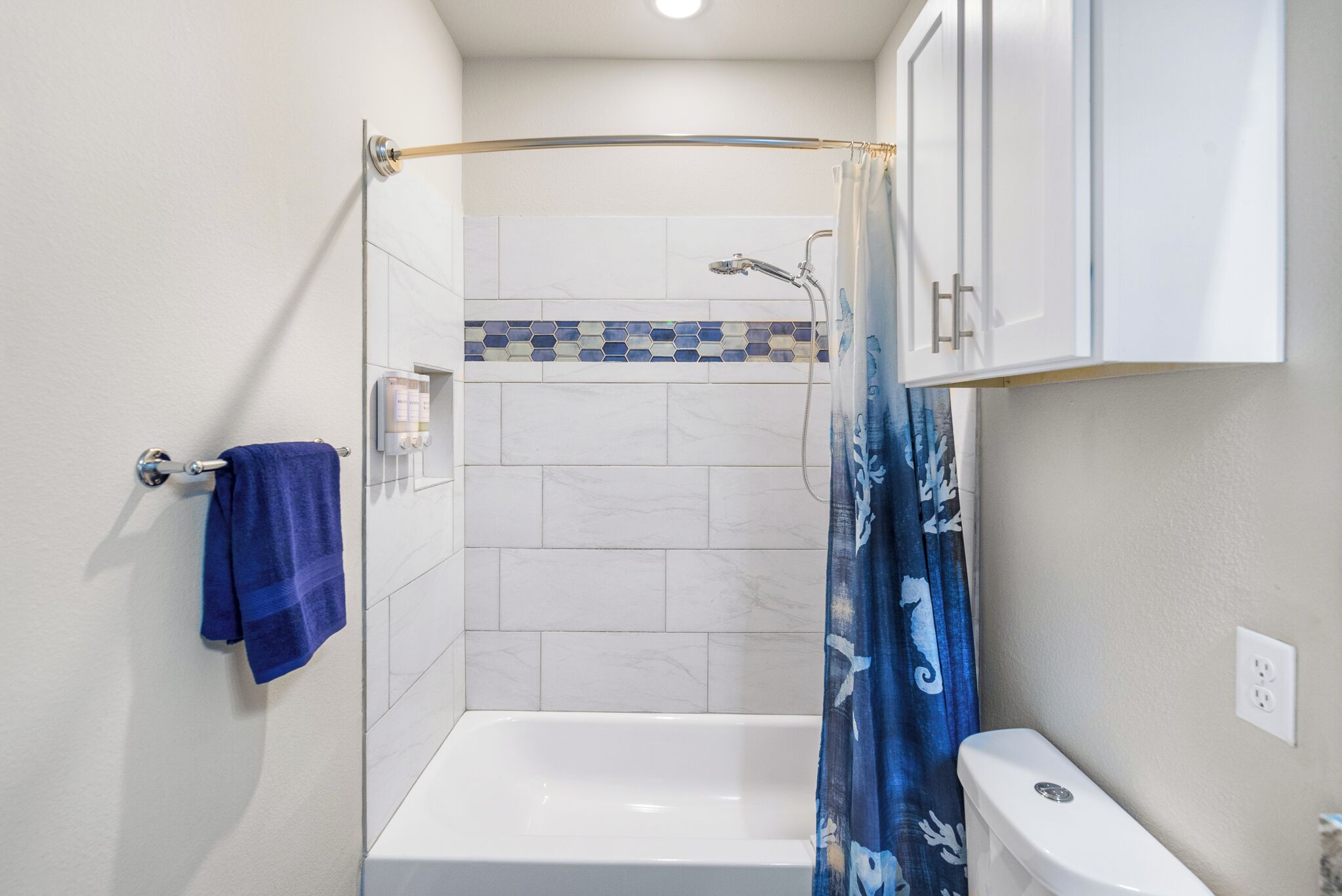 A bathroom with a white bathtub, a shower with a blue shower curtain, and a toilet.