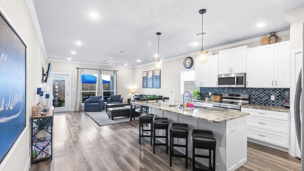A modern kitchen with white cabinets, a large island with bar stools, and a dining area with blue sofas. - PrivateHeatedPool!GameRoom!Sleeps11! (Corpus Christi)