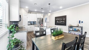 A modern kitchen with white cabinets, a stainless steel refrigerator, and a dining area with a wooden table and chairs. - PrivateHeatedPool!GameRoom!Sleeps11! (Corpus Christi)