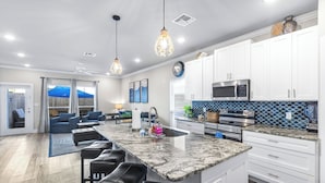 A modern kitchen with white cabinets, a large island with bar stools, stainless steel appliances, and a blue tiled backsplash. - PrivateHeatedPool!GameRoom!Sleeps11! (Corpus Christi)