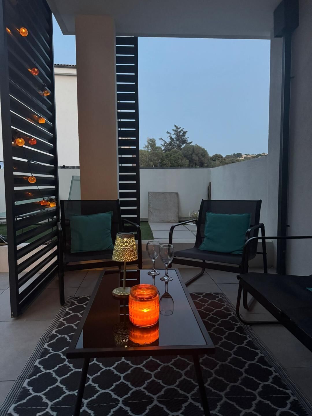 A balcony with two chairs, a table with a candle, and a lamp.