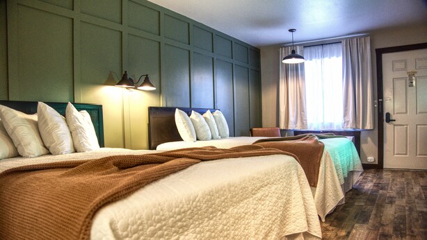 A hotel room with two beds, a wooden floor, a green wall, and a window with curtains. - New Room by Silver Dollar City + Shuttle + Pool (Branson)