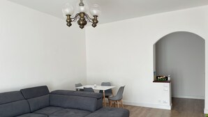 Una sala de estar moderna con un sofá seccional, una mesa de comedor con sillas y una araña.