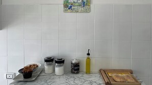 Una encimera de cocina con azulejos blancos, una cafetera, una botella de aceite y una cesta de pan.