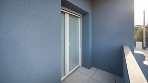 Un balcón con puerta corredera de vidrio, una lámpara sobre la puerta y piso de baldosas.