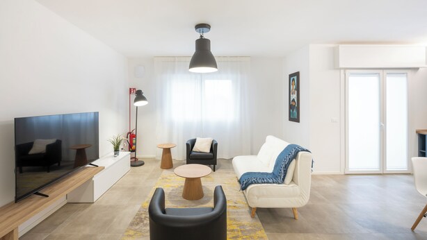 Una sala de estar moderna con un televisor de pantalla plana, un sofá, una mesa de centro y un comedor con una mesa y sillas.
