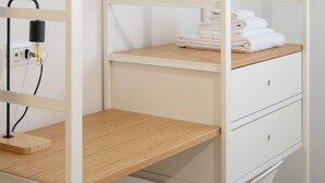 Un armario blanco con estantes de madera, un perchero de madera y un escritorio con una lámpara.