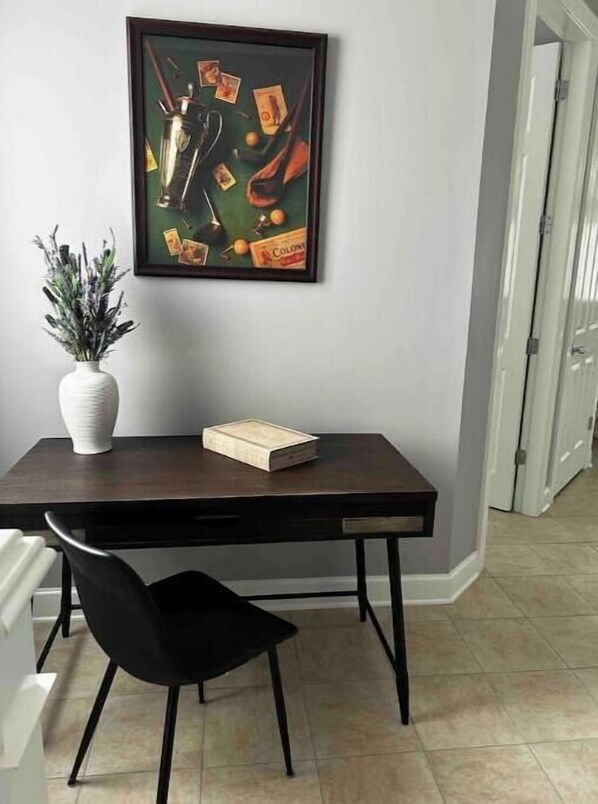 Un comedor con una mesa de madera oscura, un jarrón blanco con plantas, una silla negra y un cuadro abstracto enmarcado en la pared.