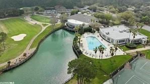 Un campo de golf con un estanque, una piscina y una casa grande con un camino de acceso circular.