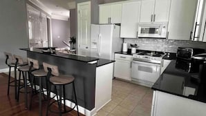Una cocina moderna con una isla central, taburetes de bar, armarios blancos y un microondas.