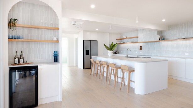 A modern kitchen with white cabinetry, a central island with bar stools, and a built-in dishwasher. - Shelby Shores (whole house) (Crescent Head)