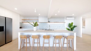 A modern kitchen with a central island, bar stools, a stainless steel refrigerator, and a potted plant. - Shelby Shores (whole house) (Crescent Head)