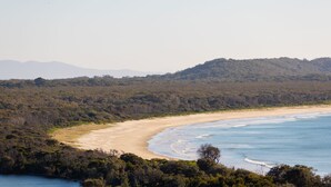 A coastal landscape with a sandy beach, dense forest, and a clear view of the ocean. - Shelby Shores (whole house) (Crescent Head)