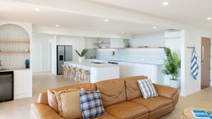 A modern kitchen with white cabinets, a central island, and bar stools. - Shelby Shores (whole house) (Crescent Head)